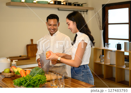 Happy couple preparing fresh fruit smoothies together in a cozy kitchen Happy couple preparing fresh fruit smoothies together in a cozy kitchen 127483793
