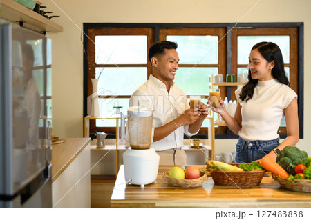 Happy couple enjoying fresh homemade smoothies together in the kitchen Happy couple enjoying fresh homemade smoothies together in the kitchen 127483838