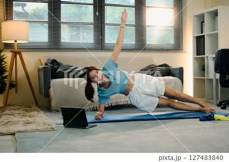 Young woman doing side plank exercise at home while following a workout video on digital tablet Young woman doing side plank exercise at home while following a workout video on digital tablet 127483840