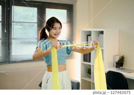 Active female stretching with a yellow resistance band during a home workout session Active female stretching with a yellow resistance band during a home workout session 127483875