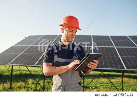 Summer time, standing and holding digital tablet. Man is doing operating and maintenance in solar power plant 127484112