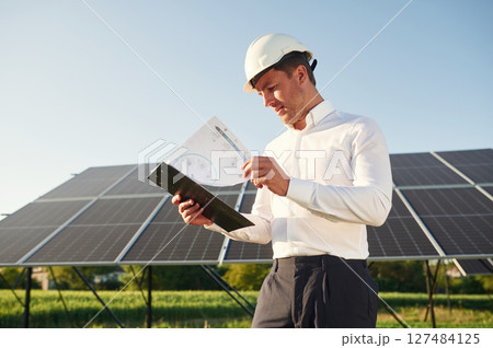 Notepad with document is in hands. Man is doing operating and maintenance in solar power plant Notepad with document is in hands. Man is doing operating and maintenance in solar power plant 127484125
