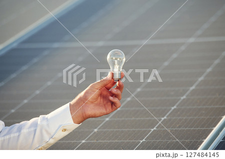 Conception of green energy. Close up view of man's hand that is holding light bult in front of solar panel 127484145