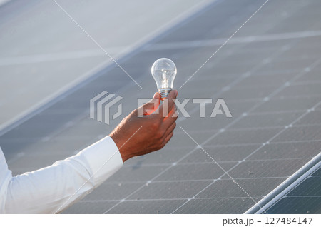 Conception of green energy. Close up view of man's hand that is holding light bult in front of solar panel 127484147
