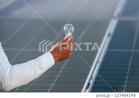 Close up view of man's hand that is holding light bult in front of solar panel Close up view of man's hand that is holding light bult in front of solar panel 127484149