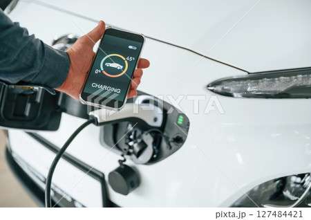 Using smartphone app for monitoring charging process. Close up view of man that is with electrical car 127484421