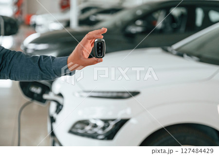 Hand is holding the keys. Close up view of man that is with electrical car 127484429