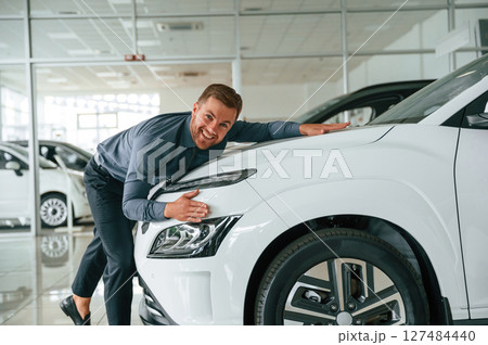 Embracing the new automobile. Handsome car dealership worker is with electric vehicle Embracing the new automobile. Handsome car dealership worker is with electric vehicle 127484440