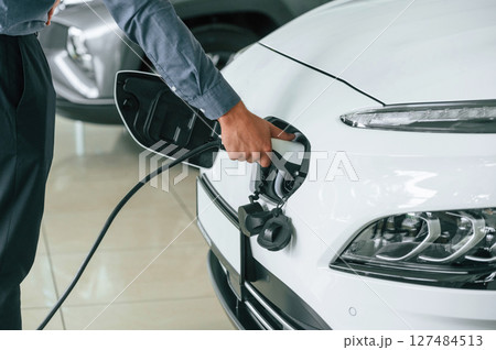 Putting charger into electrical car socket. Close up view of man Putting charger into electrical car socket. Close up view of man 127484513