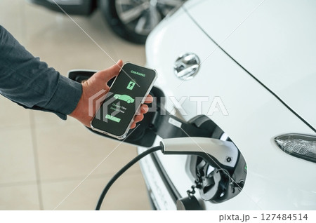Charging process on the smartphone app. Close up view of man that is with electrical car Charging process on the smartphone app. Close up view of man that is with electrical car 127484514