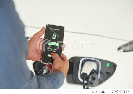 Charging process on the smartphone app. Close up view of man that is with electrical car 127484518