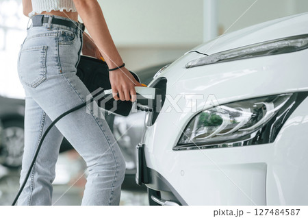 Plugging in the charger. Close up view of woman that is with electric car Plugging in the charger. Close up view of woman that is with electric car 127484587
