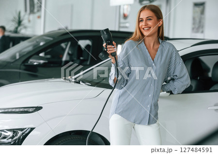 Holding charger for electric car. Beautiful woman is indoors 127484591