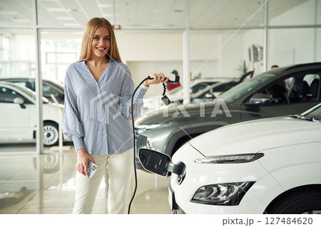 Electric car charger in hands. Beautiful woman is indoors 127484620