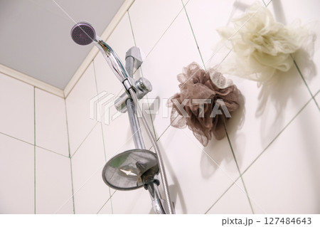 A silver shower head and a white washcloth on clean tiles in a modern bathroom, ready for a refreshing shower. Spotless white tiles frame a silver shower head and a fresh washcloth 127484643