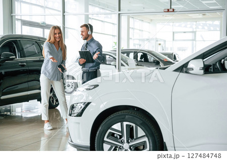 Beautiful white automobile. Man in formal clothes is with woman customer with the electric car 127484748