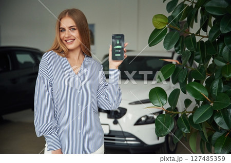 Mobile app interface of charging the electric car. Beautiful woman is indoors 127485359