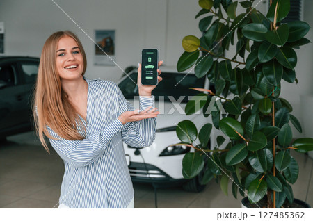 Smartphone with charging electric car app interface. Beautiful woman is indoors Smartphone with charging electric car app interface. Beautiful woman is indoors 127485362