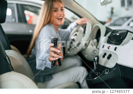 Showing the keys of new automobile. Beautiful woman is indoors with the modern car 127485377