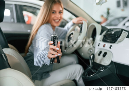 Showing the keys of new automobile. Beautiful woman is indoors with the modern car 127485378