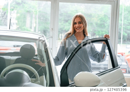 Door is opened, standing. Beautiful woman is indoors with the modern car Door is opened, standing. Beautiful woman is indoors with the modern car 127485396
