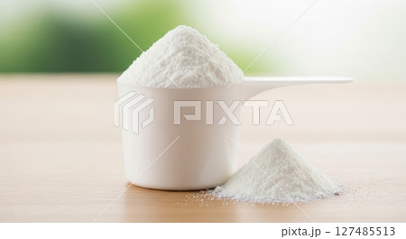 White protein powder in a measuring scoop on a wooden table with green background 127485513