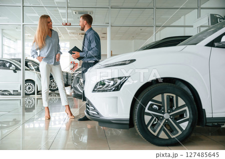 Choosing the automobile. Man in formal clothes is with woman customer with the electric car Choosing the automobile. Man in formal clothes is with woman customer with the electric car 127485645