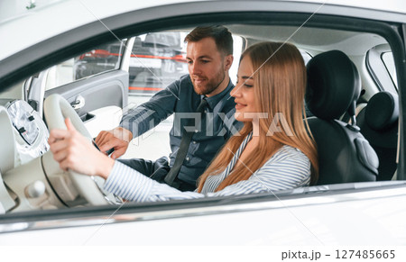 Explaining how automobile works. Man in formal clothes is with woman customer with the electric car Explaining how automobile works. Man in formal clothes is with woman customer with the electric car 127485665