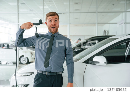 Having fun with charger. Handsome car dealership worker is with electric vehicle Having fun with charger. Handsome car dealership worker is with electric vehicle 127485685