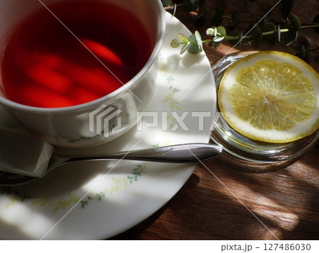 日差しのかかるテーブル上の、カップに注がれたホットティー(レモン、角砂糖添え) 日差しのかかるテーブル上の、カップに注がれたホットティー(レモン、角砂糖添え) 127486030