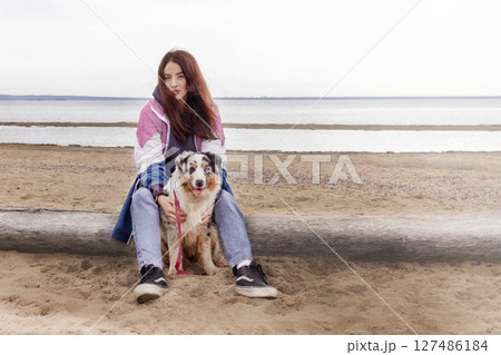 Caucasian brunete woman sit with blue merle Australian shepherd dog on a beach copy space 127486184