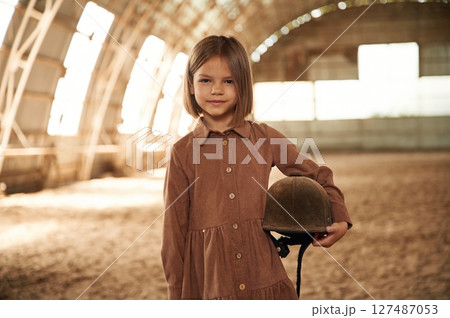 Little girl in jockey clothes is standing indoors 127487053