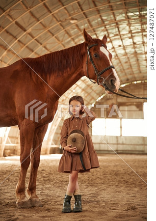 Standing with the animal. Cute little girl is with horse indoors Standing with the animal. Cute little girl is with horse indoors 127487071