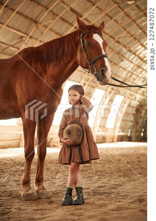 Standing with the animal. Cute little girl is with horse indoors Standing with the animal. Cute little girl is with horse indoors 127487072
