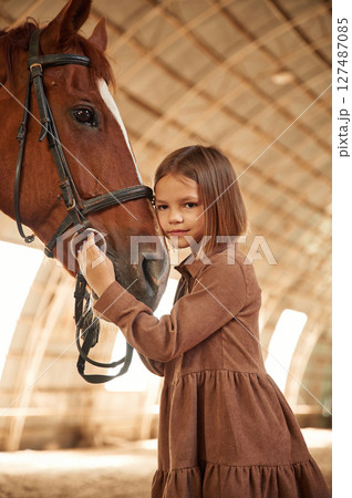 Cute little girl is with horse indoors 127487085