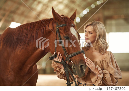 Front view. Beautiful young woman is with horse indoors Front view. Beautiful young woman is with horse indoors 127487202
