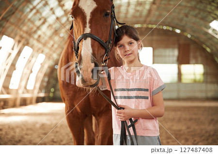 Portrait of cute little girl that is with horse indoors Portrait of cute little girl that is with horse indoors 127487408