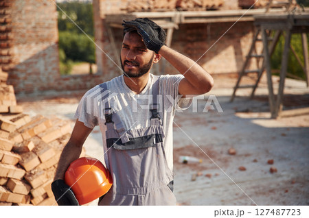 In grey uniform. Handsome Indian man is on the construction site In grey uniform. Handsome Indian man is on the construction site 127487723