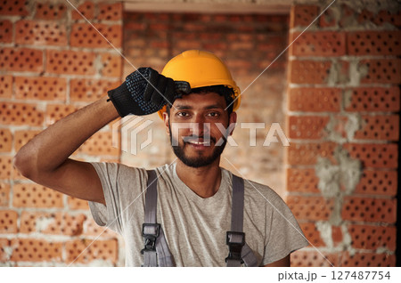 Indoors against brick wall. Handsome Indian man is on the construction site Indoors against brick wall. Handsome Indian man is on the construction site 127487754