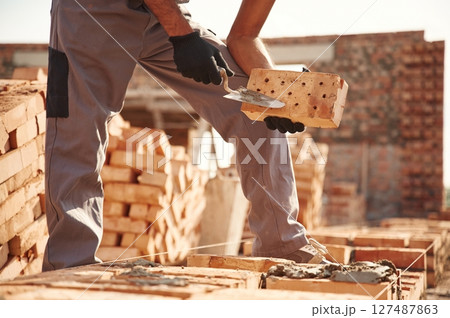 With brick in hands. Close up view of man that is working on the construction site 127487863