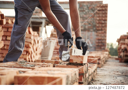 In gloves, holding brick. Close up view of man that is working on the construction site In gloves, holding brick. Close up view of man that is working on the construction site 127487872