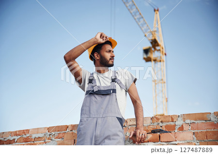 Taaking a break. Standing against crane and blue sky. Handsome Indian man is on the construction site 127487889