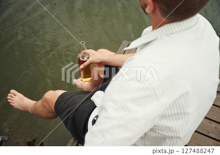 Close up view of man that is sitting by the water with beer in hands 127488247
