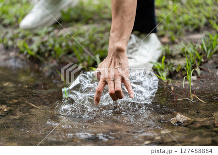 Volunteer action. Individual retrieving plastic bottle from river. 127488884
