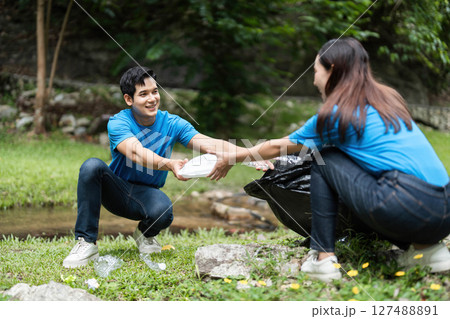 Volunteer Team Collecting Waste in Nature. Two individuals engaged in a cleanup effort in a lush setting. Volunteer Team Collecting Waste in Nature. Two individuals engaged in a cleanup effort in a lush setting. 127488891