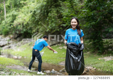Volunteer teamwork. Young woman and man cleaning up a stream. Volunteer teamwork. Young woman and man cleaning up a stream. 127488895