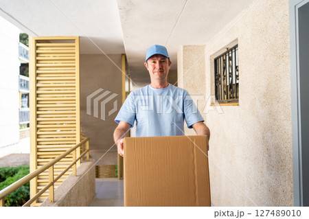 A male courier in a blue uniform with a parcel in his hands. A male courier in a blue uniform with a parcel in his hands. 127489010