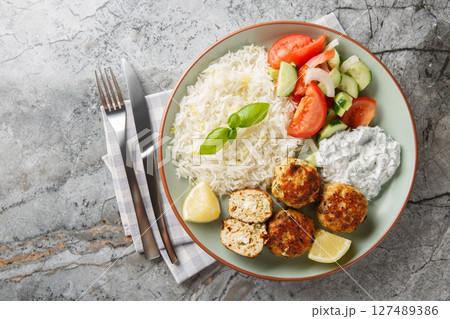 Delicious chicken meatballs stuffed with feta cheese served with lemon rice, tzatziki sauce and vegetable salad close-up in a plate. horizontal top view 127489386