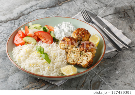 Spicy Greek Chicken meatballs stuffed with feta cheese served with lemon rice, tzatziki sauce and fresh salad close-up in a plate. horizontal 127489395