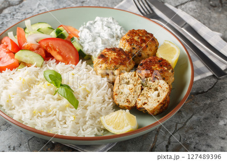 Delicious chicken meatballs stuffed with feta cheese served with lemon rice, tzatziki sauce and vegetable salad close-up in a plate. horizontal 127489396